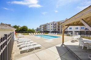 A pool area with lounge chairs and a covered seating area. - Rogue KDH steps to the  Beach condo w/ pool (Kill Devil Hills)