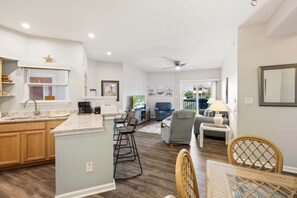 A modern kitchen with a central island, a dining area with a table and chairs, a living room with a sofa and armchairs, and a balcony with a railing. - Rogue KDH steps to the  Beach condo w/ pool (Kill Devil Hills)