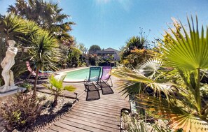 A wooden deck leading to a swimming pool surrounded by tropical plants and a statue. - Stunning home in Saint-Laurent-d'Aigouz (Saint-Laurent-d'Aigouz)