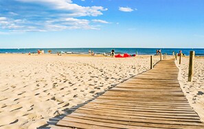 Een houten vlonder die naar een zandstrand leidt, met mensen in de verte.