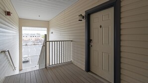 Ein überdachter Balkon mit einer weißen Tür, einem Geländer und Blick auf einen Parkplatz.