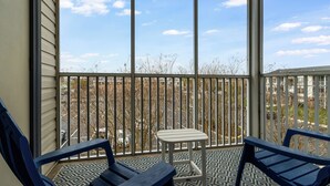 Ein Balkon mit zwei blauen Stühlen, einem kleinen weißen Tisch und einem gemusterten Boden.