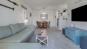 Ein Wohnzimmer mit grauem Sofa, einem Couchtisch, einem Esstisch mit Stühlen, einem Fernseher und einem Schrank.