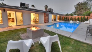 Ett modernt hus med en swimmingpool, utomhusmöbler och en eldstad.