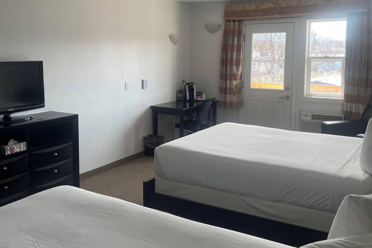 A hotel room with two beds, a desk with a chair, a television, and a window with curtains.
