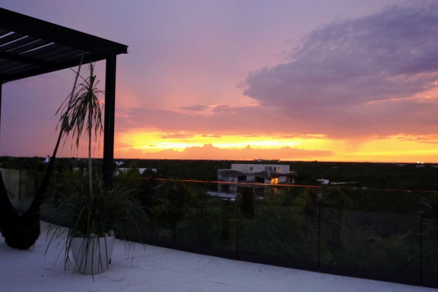 A balcony with a view of a sunset over a landscape, including a building and vegetation.