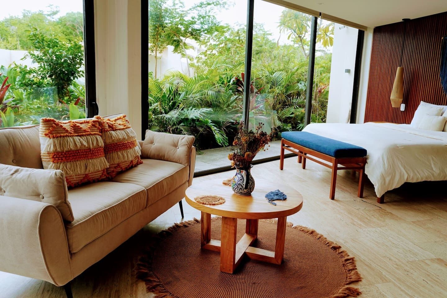 Une chambre moderne avec un canapé, un lit, une petite table et une vue sur une végétation luxuriante.