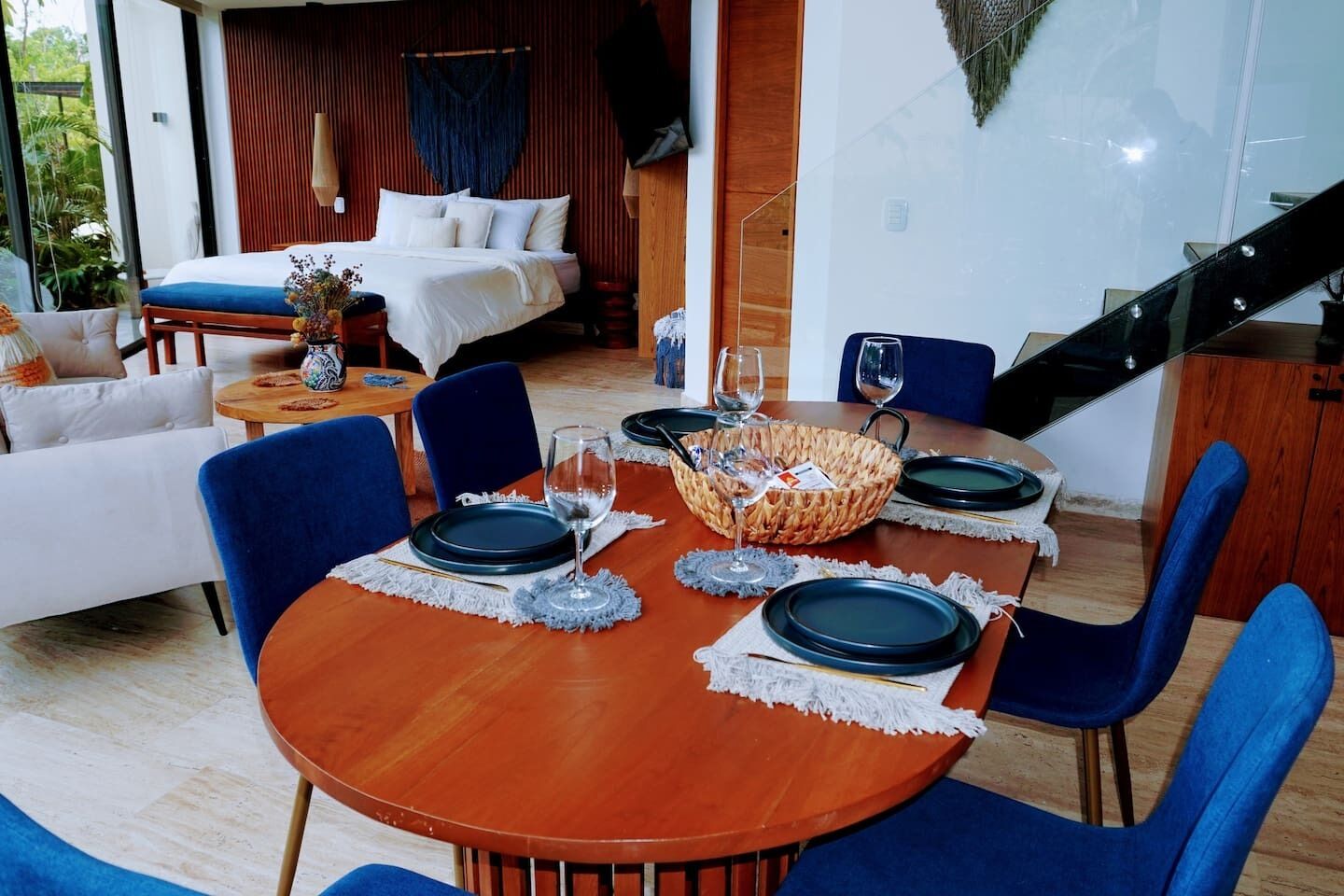 A dining area with a wooden table set for four, blue chairs, and a woven basket centerpiece.