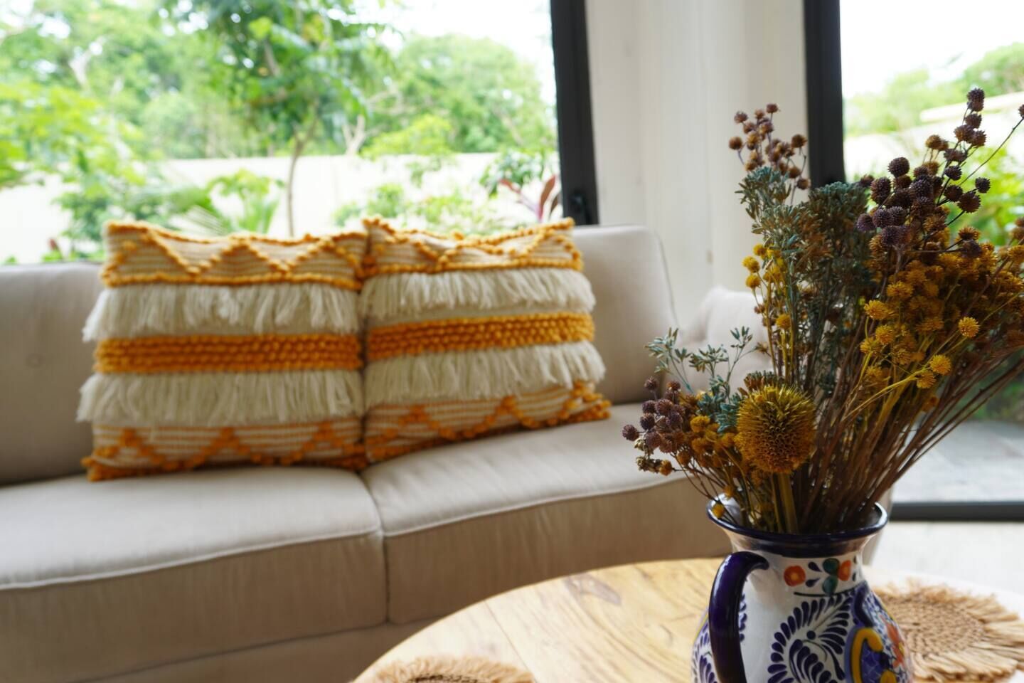 A sofa with patterned cushions and a vase with dried flowers on a table.