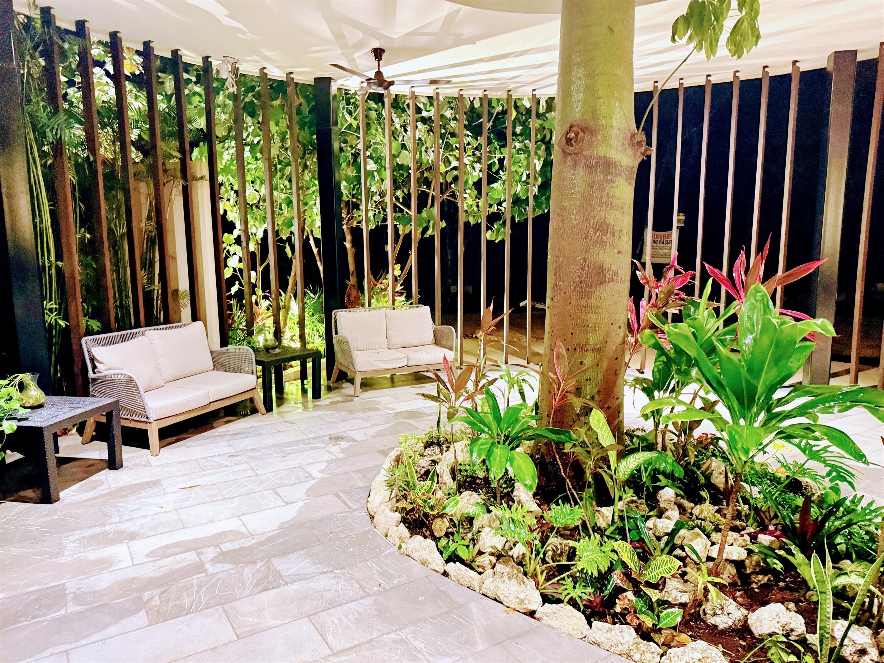 A covered outdoor seating area with two sofas, a small table, and a variety of plants.