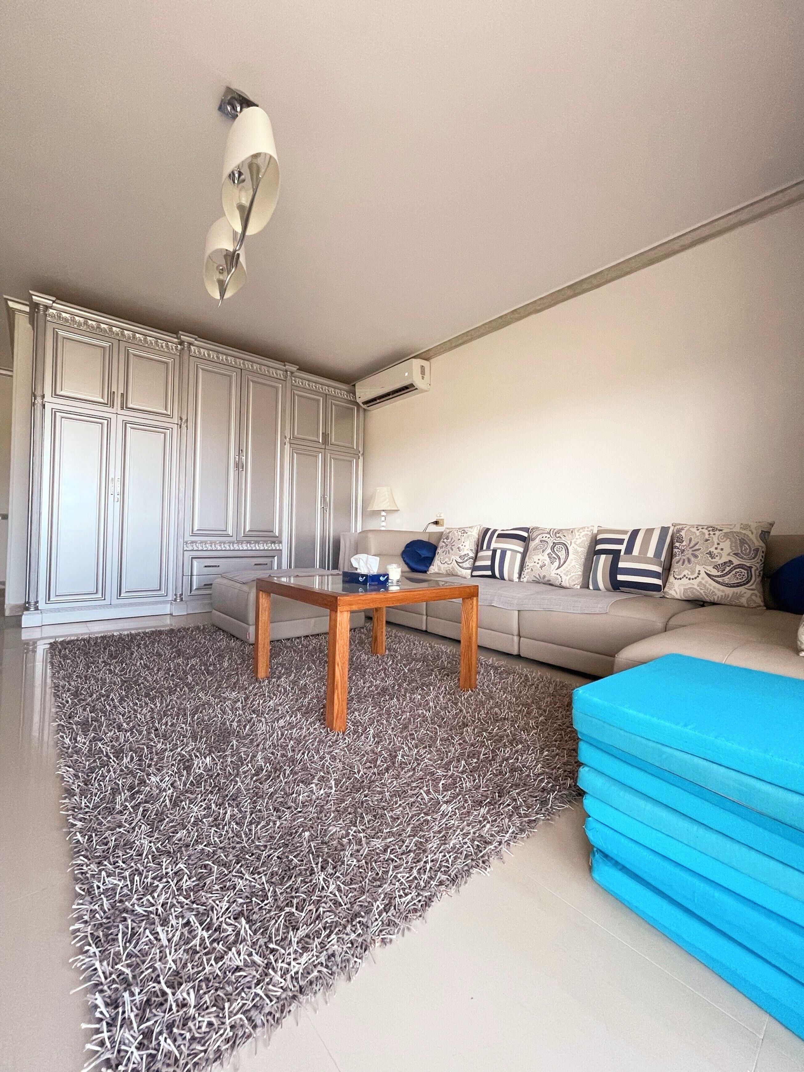 Ein Wohnzimmer mit einer Couch, einem Couchtisch, einem gemusterten Teppich und einem blauen Hocker.