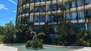 Een hotel met meerdere verdiepingen, voorzien van balkons, een zwembad en weelderige beplanting.