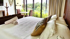 Hotelkamer met een groot bed, uitzicht op groen, een klein tafeltje en een stoel.