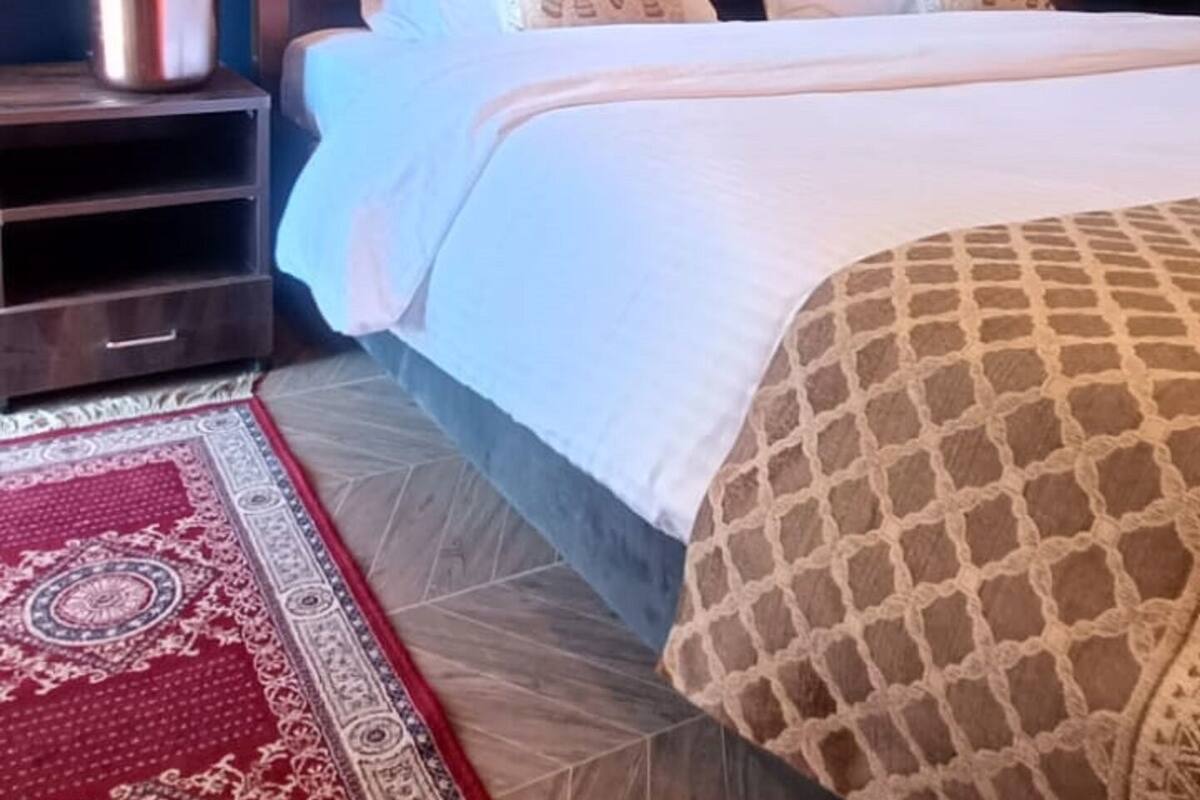 A bedroom with a tufted headboard, a red patterned rug, and a white bedspread.