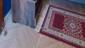 A bedroom with a bed, a nightstand with a vase of flowers, a wall-mounted lamp, a wardrobe, and a patterned rug. - KAY'S EDEN (Mahabalipuram)