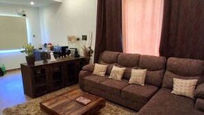 A living room with a sectional sofa, a coffee table, a TV, and a ceiling fan. - KAY'S EDEN (Mahabalipuram)