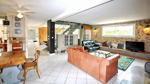 Een ruime woonkamer met een eettafel, stoelen, een bank, een televisie en een trap naar een ander niveau.