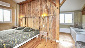 Een slaapkamer met een houten hoofdbord, een bed met bloemenbeddengoed, een klein houten kistje en een raam.