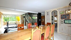 Een eetgedeelte met een houten tafel, rode fauteuils, een trap en uitzicht op groen buiten.
