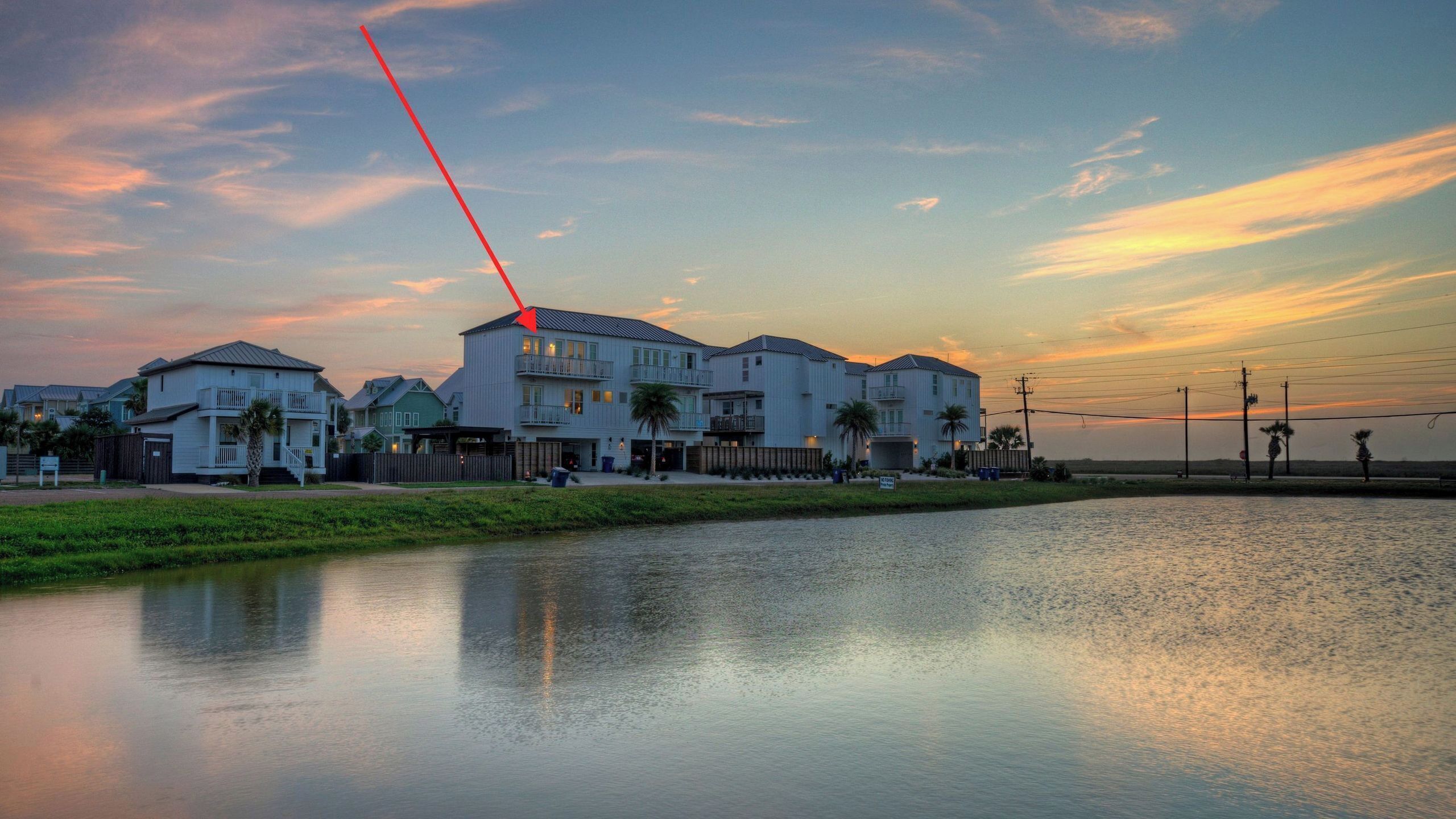 A waterfront residential area with multiple houses, a calm body of water, and a sunset sky.