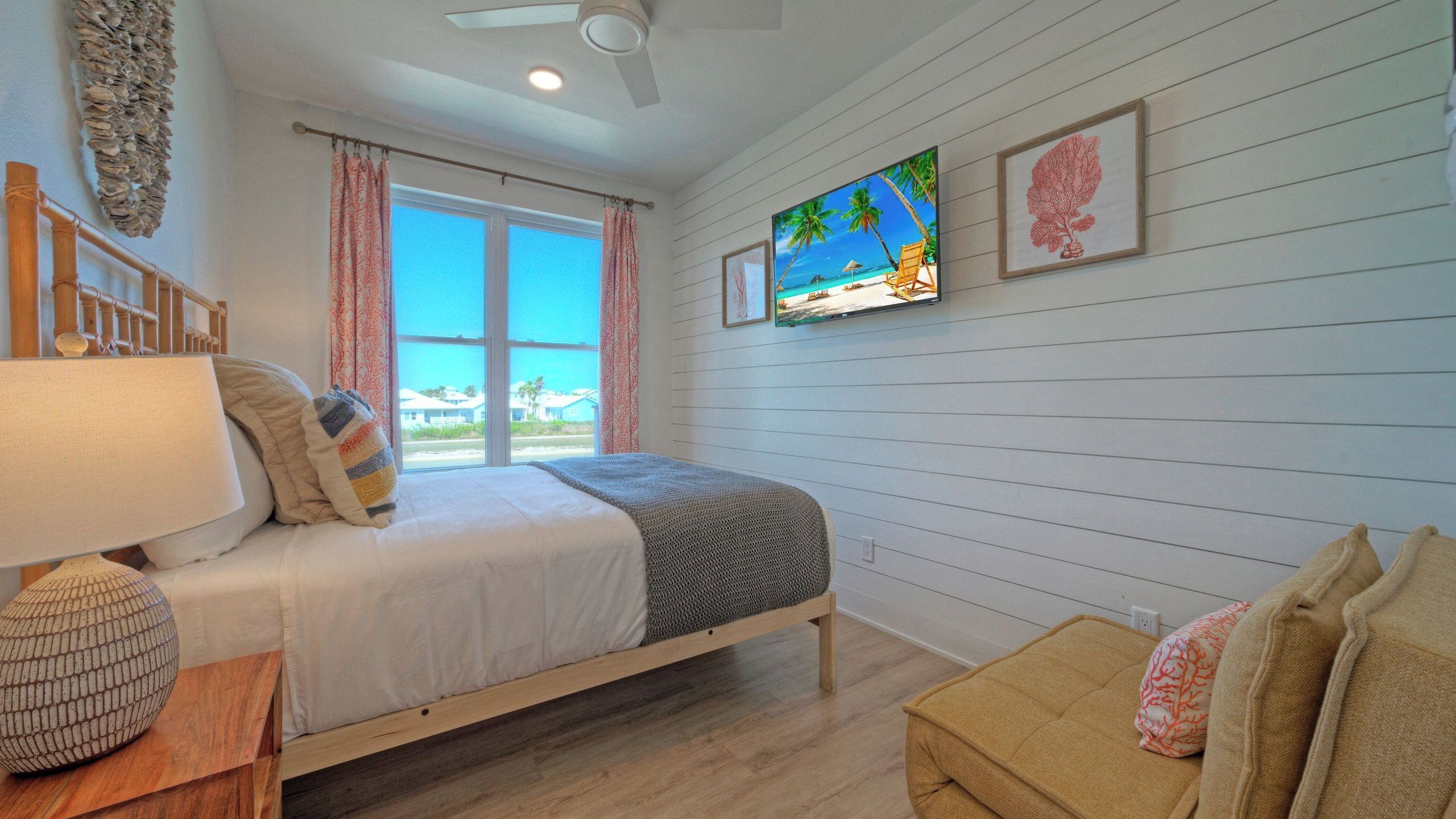 Un dormitorio con cama, televisor, piso de madera y ventana con cortinas.