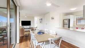 A modern apartment with a dining area, kitchen, and a large window. - Sunset Reset - Bright Coastal Escape (Soldiers Point)