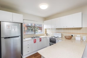 A modern kitchen with stainless steel appliances, a granite countertop, and a view of the outside. - Sunset Reset Beachfront in Soldiers Point (Soldiers Point)