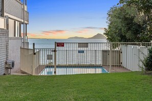 A swimming pool with a gate, a clear view of the sea, and a mountain in the background. - Sunset Reset Beachfront in Soldiers Point (Soldiers Point)