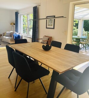 A modern dining area with a wooden table and black chairs, a sofa, and a window with curtains.