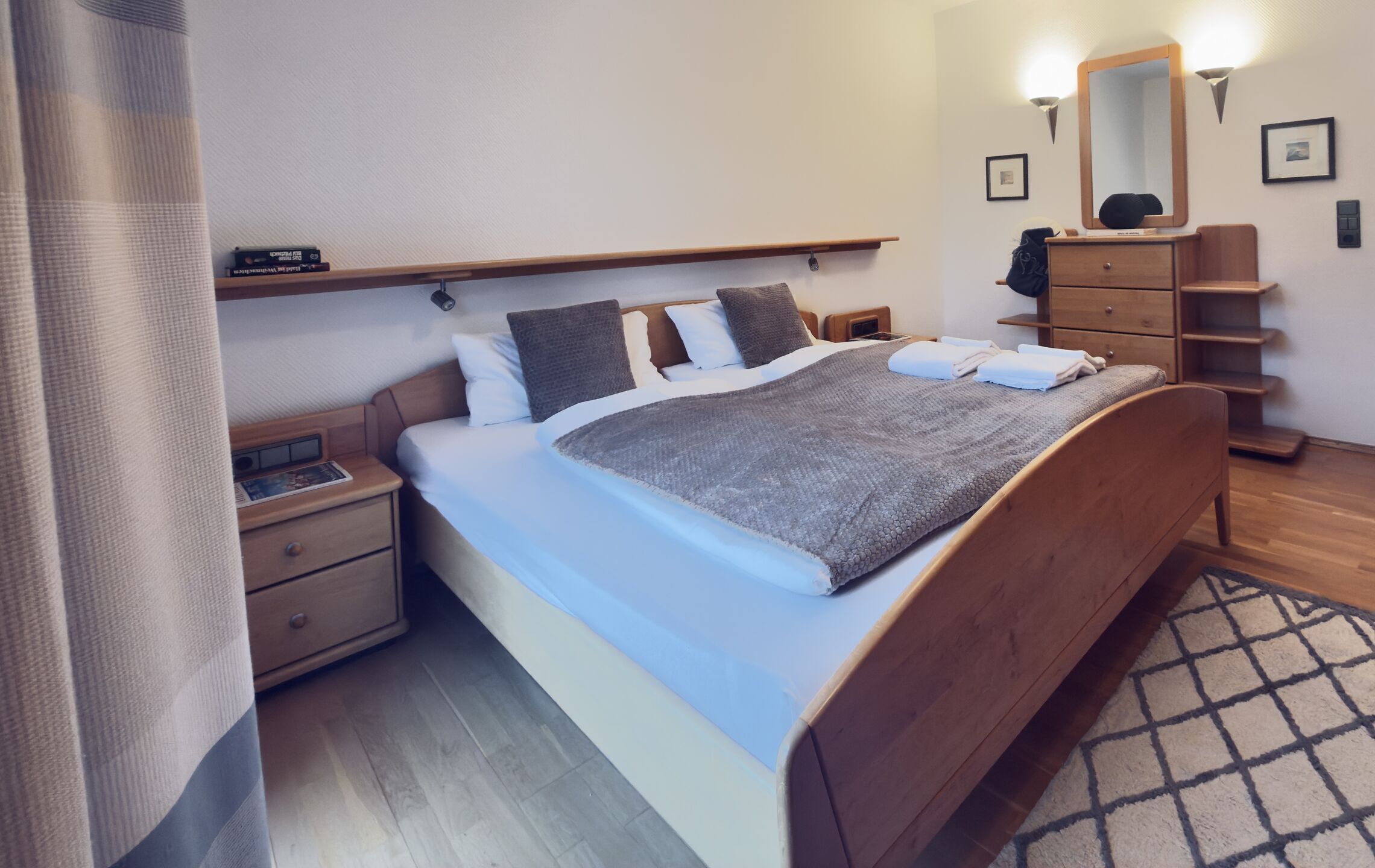 A neatly arranged bedroom with a bed, bedside tables, a dresser, a mirror, and a shelf.