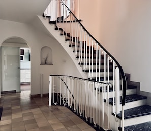 A modern staircase with a black handrail and white balusters, leading to a landing with a door and a small window.