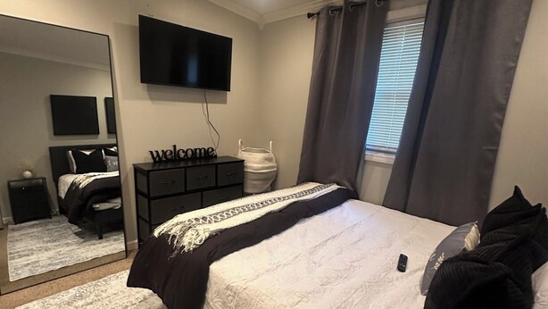 Quarto com uma cama, televisão na parede, mesa de cabeceira, espelho e janela com cortinas.