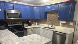 A kitchen with blue cabinets, a stainless steel microwave, a stove, and a dishwasher.