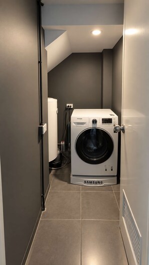 Ein kleiner Waschraum mit einer Samsung Waschmaschine, einem kleinen Kühlschrank und einem gefliesten Boden.