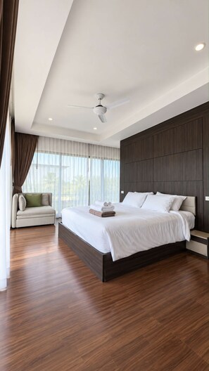 A modern bedroom with a large bed, a ceiling fan, and a view of the outdoors through the window. - 2BR Pool Villa Rawai Beach Sumalee | Capital Pro (Rawai)