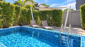 Ein Swimmingpool mit blauen Kacheln, umgeben von viel Grün und einem modernen Gebäude.