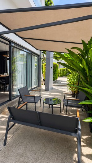 An outdoor seating area with modern furniture, a glass wall, and potted plants. - 2BR Pool Villa Rawai Beach Sumalee | Capital Pro (Rawai)