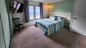 Une chambre à coucher avec un lit, une chaise, un téléviseur fixé au mur et une fenêtre avec des rideaux.