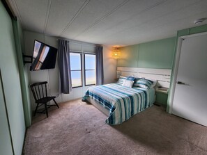 A bedroom with a bed, a chair, a TV mounted on the wall, and a window with curtains.