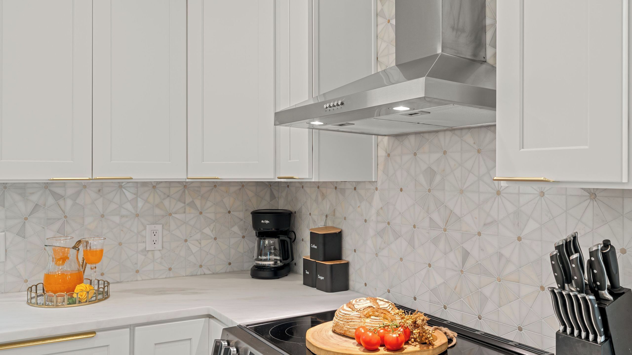 A modern kitchen with white cabinets, a stainless steel range hood, a coffee maker, and a knife block.
