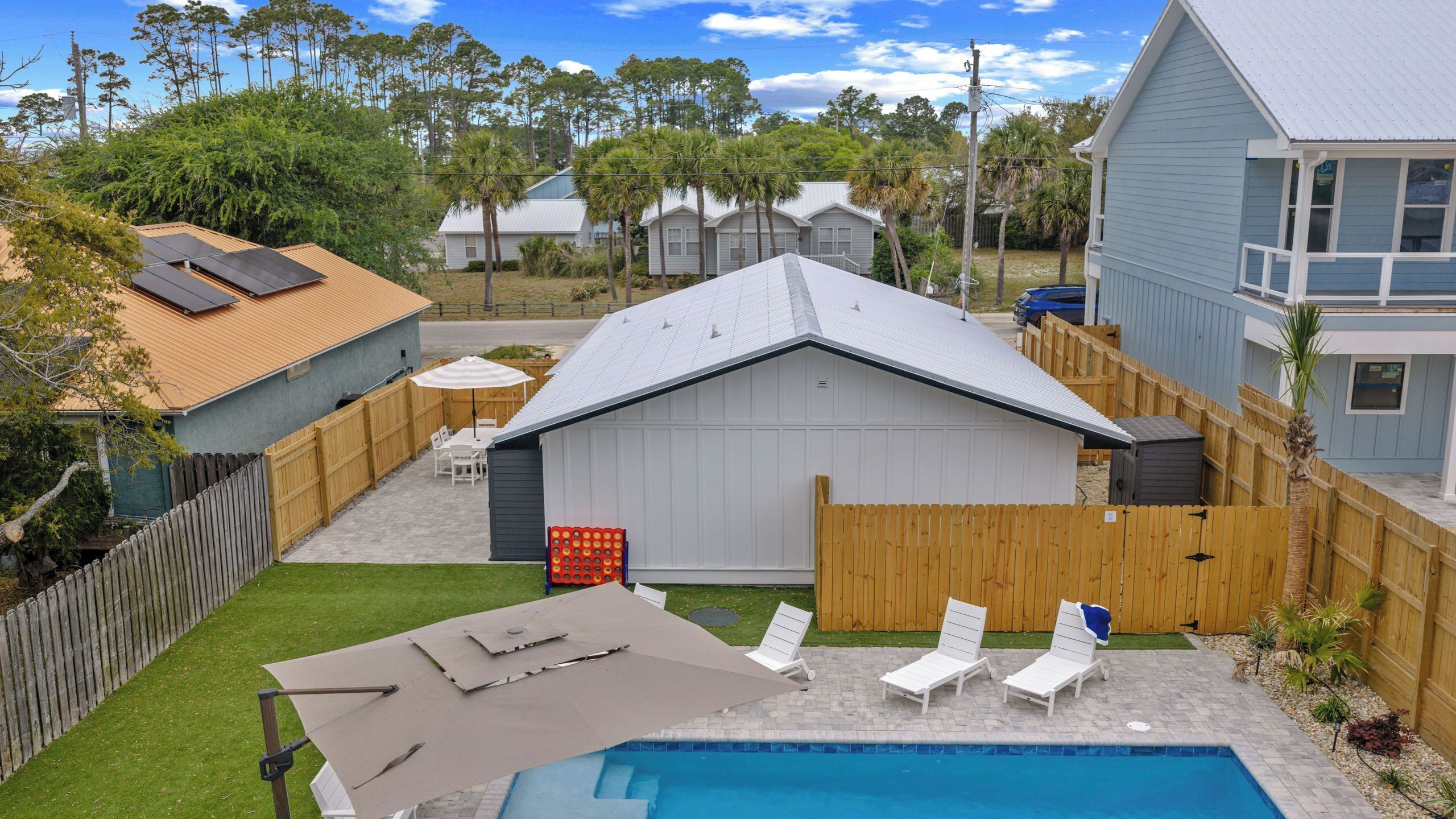 A backyard with a swimming pool, a covered patio, and a fenced area.