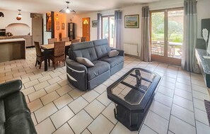 Una sala de estar con sofá, una mesa de centro de vidrio, una zona de comedor con mesa y sillas, y una cocina al fondo.