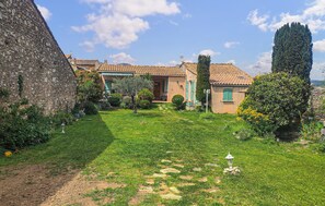Un muro de piedra, una casa con techo de tejas y un jardín bien cuidado.