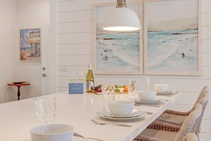 A dining area with a white table set for four, a wine bottle, and a fruit basket.