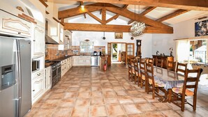 A spacious kitchen with modern appliances, a dining area with wooden chairs, and a rustic ceiling. - Authentique maison piscine (Laroque Des Albères)