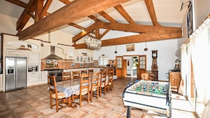 A spacious kitchen with wooden beams, a dining area with chairs, a foosball table, and a refrigerator. - Authentique maison piscine (Laroque Des Albères)