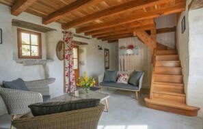 Ein rustikales Interieur mit freiliegenden Holzbalken, einer Couch, Korbmöbeln und einer Treppe.