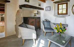 Ein Zimmer mit einem Korbsessel, einem grauen Sessel, einem kleinen Tisch mit Blumenvase und einem Holzschrank.