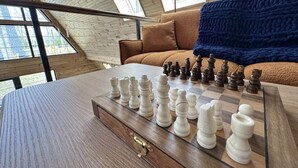 A chessboard on a wooden table in a room with a sloped ceiling and a view of the outdoors. - A-Frame Escape | Firepit Nights + Lake Days (Coolbaugh Township)
