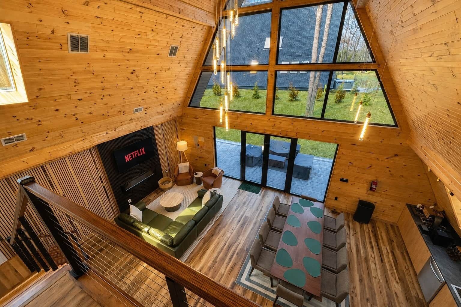 A wooden cabin interior with a fireplace, seating area, and large windows overlooking a garden.